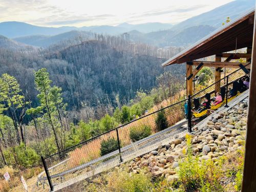 A scenic view of mountains and valleys, with a wooden structure and a path leading down, surrounded by greenery.