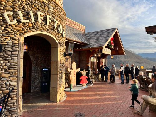A stone building with "CLIFFTOP" sign, people gathered outside, and a gingerbread figure in front, with mountains in the background.