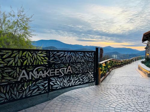 A decorative gate with "Anakeesta" signage opens to a scenic pathway and mountains under a cloudy sky at sunset.