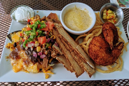 A plate of nachos topped with meat, vegetables, and cheese, alongside shrimp, bread, and a small bowl of sauce.