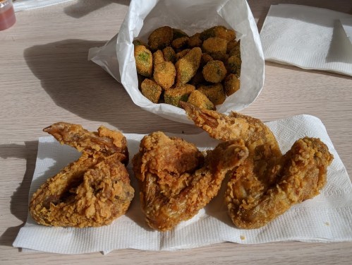 A plate with three crispy fried chicken wings and a bag of fried okra on a table.