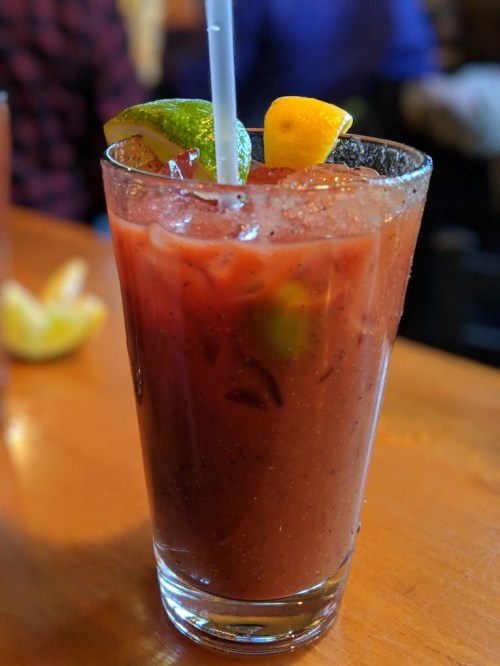 A tall glass of a colorful cocktail garnished with lime and lemon slices, served on a wooden table.