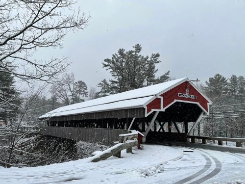 A red covered bridge in a snowy landscape, surrounded by trees and falling snowflakes.