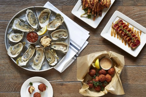 A seafood spread featuring oysters on a platter, tuna, fried balls, and a side of dipping sauce.