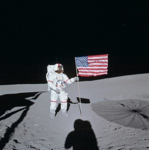 An astronaut stands on the moon, holding an American flag against a dark, starry background.