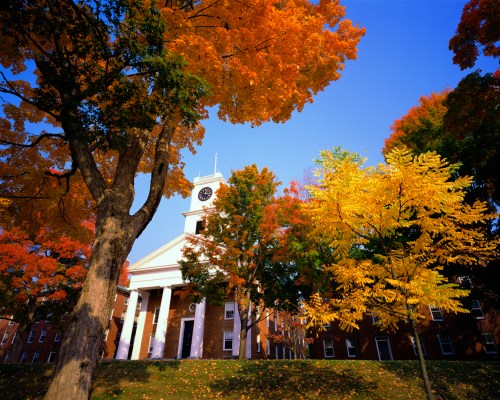 A historic building surrounded by vibrant autumn trees in shades of orange and yellow against a clear blue sky.