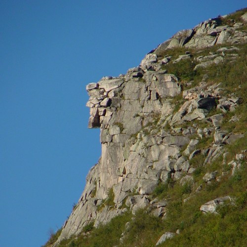 A rocky cliff formation resembling a lion's head against a clear blue sky.