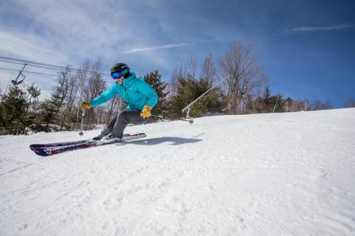 A skier in a blue jacket and helmet glides down a snowy slope under a clear blue sky.