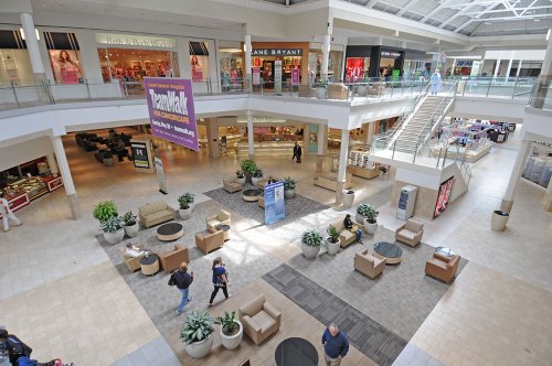 A spacious mall interior with seating areas, shops, and shoppers walking around. Bright and open atmosphere.