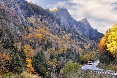 A winding road through a colorful autumn landscape with mountains and trees in vibrant fall foliage.