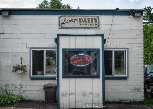 A small, white building with a blue trim sign reading "Larry's Pasty Shop" and an illuminated "OPEN" sign in the window.