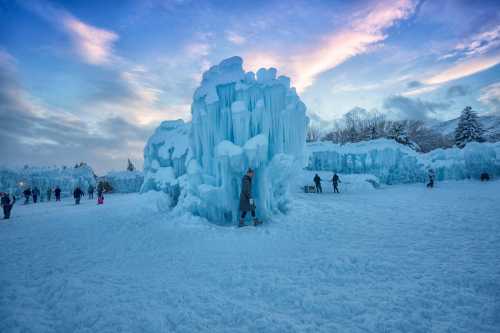 A snowy landscape featuring towering ice formations and people exploring the winter scene under a colorful sky.