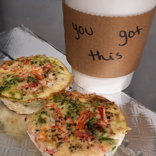 A coffee cup with a motivational message next to a plate of colorful vegetable frittatas.
