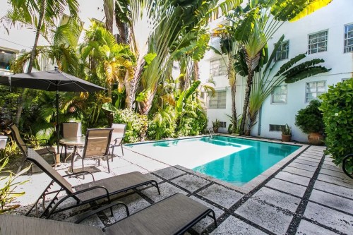 A serene pool area surrounded by lush greenery and palm trees, featuring lounge chairs and an umbrella.