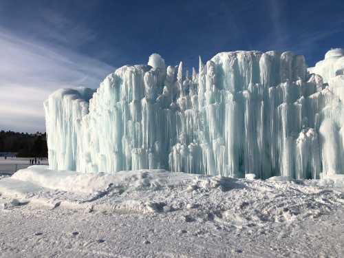 A large, icy formation with towering blue icicles against a clear sky, surrounded by snow.