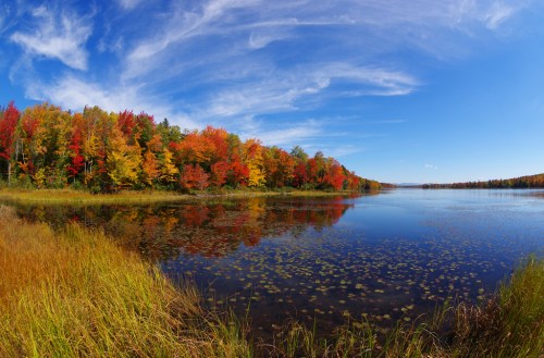 A serene lake surrounded by vibrant autumn foliage and a clear blue sky, reflecting colorful trees in the water.