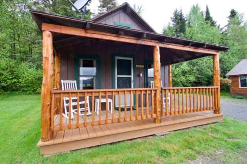 A cozy cabin with a wooden porch, rocking chairs, and surrounded by greenery.