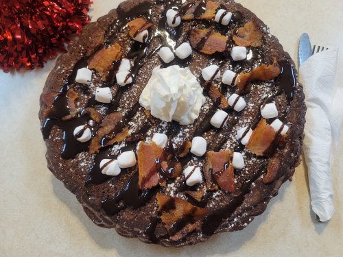 A chocolate dessert topped with whipped cream, marshmallows, and drizzled with chocolate sauce, on a festive table.