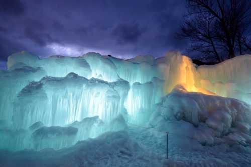 Illuminated ice formations glow in shades of blue and orange against a dark, cloudy sky.