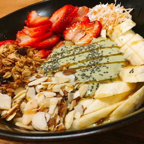 A bowl of smoothie topped with sliced bananas, strawberries, granola, almonds, chia seeds, and a drizzle of honey.