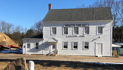 A white two-story building with "Middleton Town Hall" and "Welcome Home" signs, surrounded by a snowy landscape.
