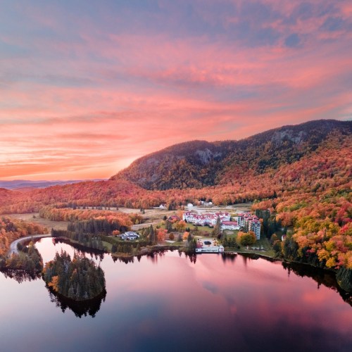 Aerial view of a serene landscape with colorful autumn trees, a calm lake, and a small resort nestled in the hills.