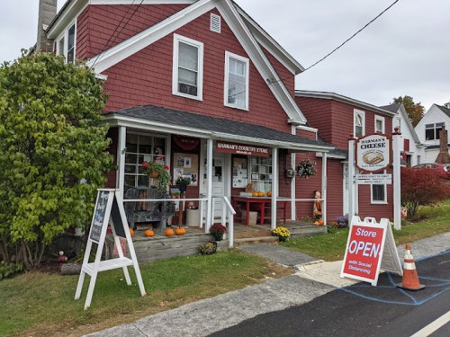 A charming red country store with pumpkins outside, featuring a sign that says "Store OPEN with Social Distancing."