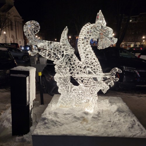 An intricate ice sculpture of a dragon, illuminated and surrounded by snow, set in an outdoor winter scene.