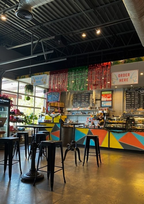 A colorful café interior with a counter, menu boards, and seating, featuring festive decorations and a welcoming atmosphere.