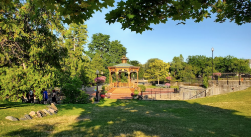 A scenic park with a gazebo surrounded by greenery and flowers, featuring a grassy area and a peaceful atmosphere.