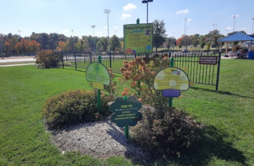Colorful signs in a park garden area, with a playground in the background and trees showing autumn colors.