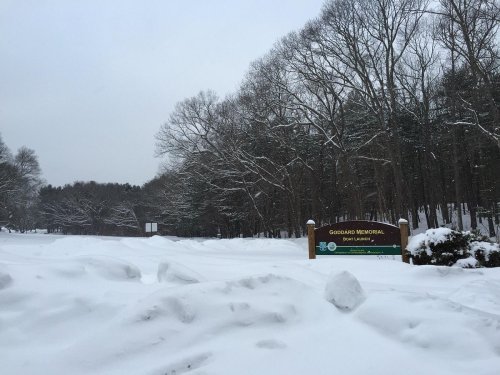 Snow-covered landscape with trees and a sign for "Goodrich Memorial" partially visible in a winter scene.