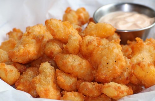 A close-up of golden, crispy fried bites served with a small bowl of dipping sauce.