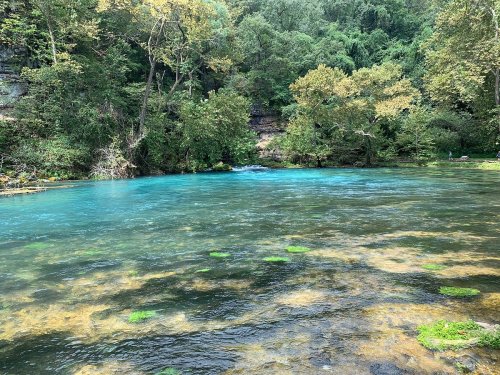 A serene river with turquoise water surrounded by lush green trees and rocky banks.