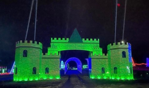 A brightly lit green castle entrance with towers, surrounded by colorful lights in a festive night setting.