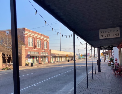 A quiet street scene featuring storefronts and string lights, with a clear blue sky above.