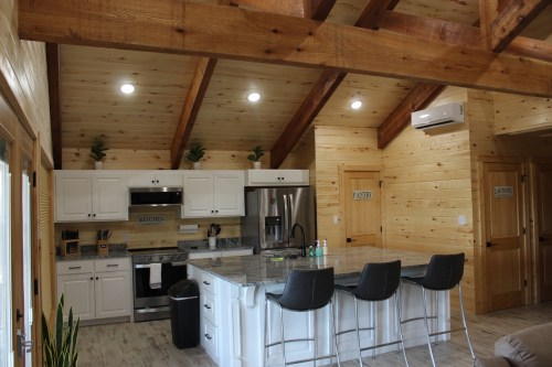 Modern kitchen with wooden beams, granite island, stainless steel appliances, and bar stools. Bright and inviting space.