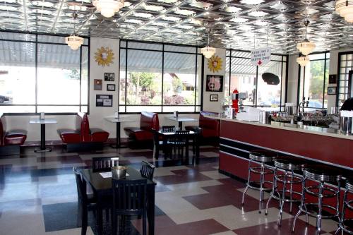 A retro diner interior with red booths, black tables, and a shiny ceiling, featuring a counter and large windows.