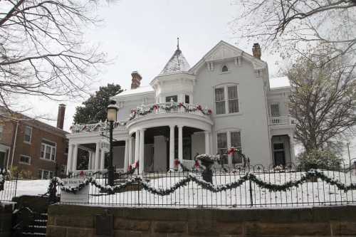 A large white Victorian house decorated for Christmas, surrounded by snow and festive garlands.