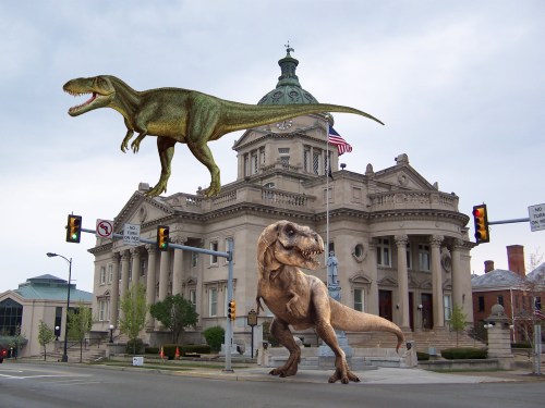 Two large dinosaurs, including a T. rex, are superimposed over a historic building in an urban setting.