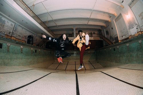 Two people jumping in an empty, vintage swimming pool, showcasing dynamic poses and stylish outfits.