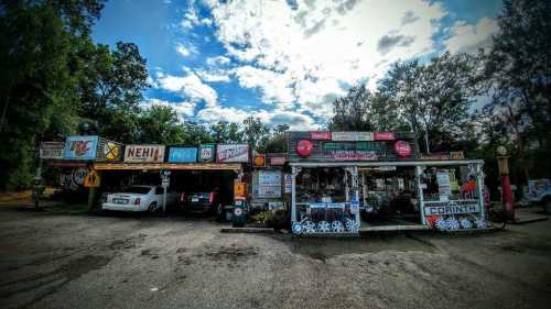 A quirky roadside shop with vintage signs, cars parked outside, and a cloudy sky overhead.