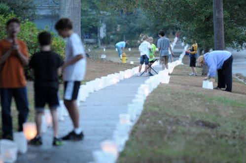 Children and adults set up glowing lanterns along a sidewalk in a neighborhood during an evening event.