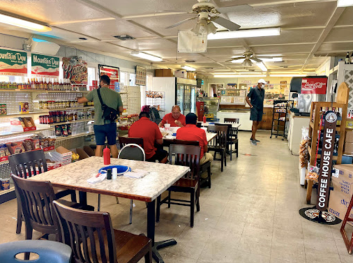 A casual café interior with tables, patrons in red shirts, and shelves stocked with snacks and drinks.