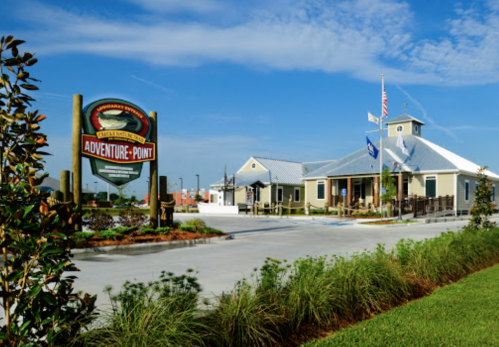 A building with a sign reading "Adventure Point," surrounded by greenery and a clear blue sky.