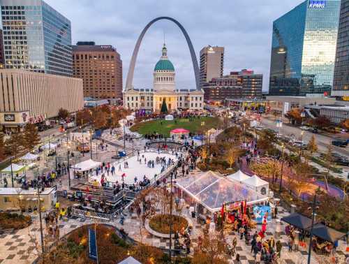 Aerial view of a bustling ice skating rink in a city plaza, with the iconic arch and historic building in the background.