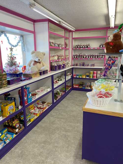 A colorful candy shop with shelves filled with sweets, a teddy bear, and festive decorations.