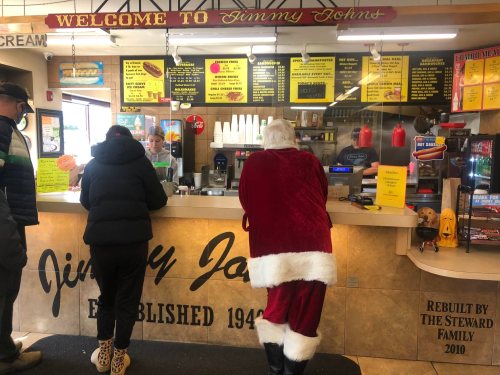 A Santa-clad customer stands at the counter of Jimmy John's, with two other patrons ordering food.