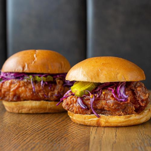 Two crispy fried chicken sandwiches with pickles and purple cabbage on soft buns, placed on a wooden table.