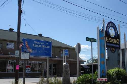 A street view featuring a "Welcome to Rhode Island" sign and a business sign for "Gateway" on a sunny day.